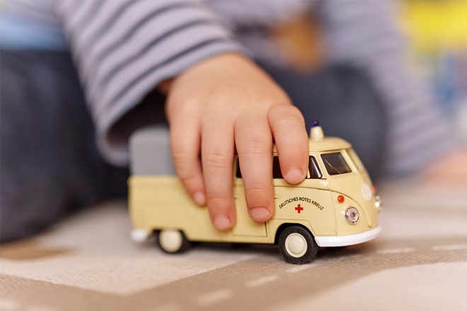 Kinderhand schiebt Spielzeugauto VW Bulli