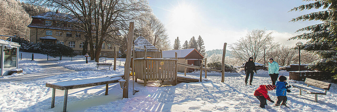 Blick auf den verschneiten Spielplatz der Kureinrichtung, im Vordergrund spielende Kinder